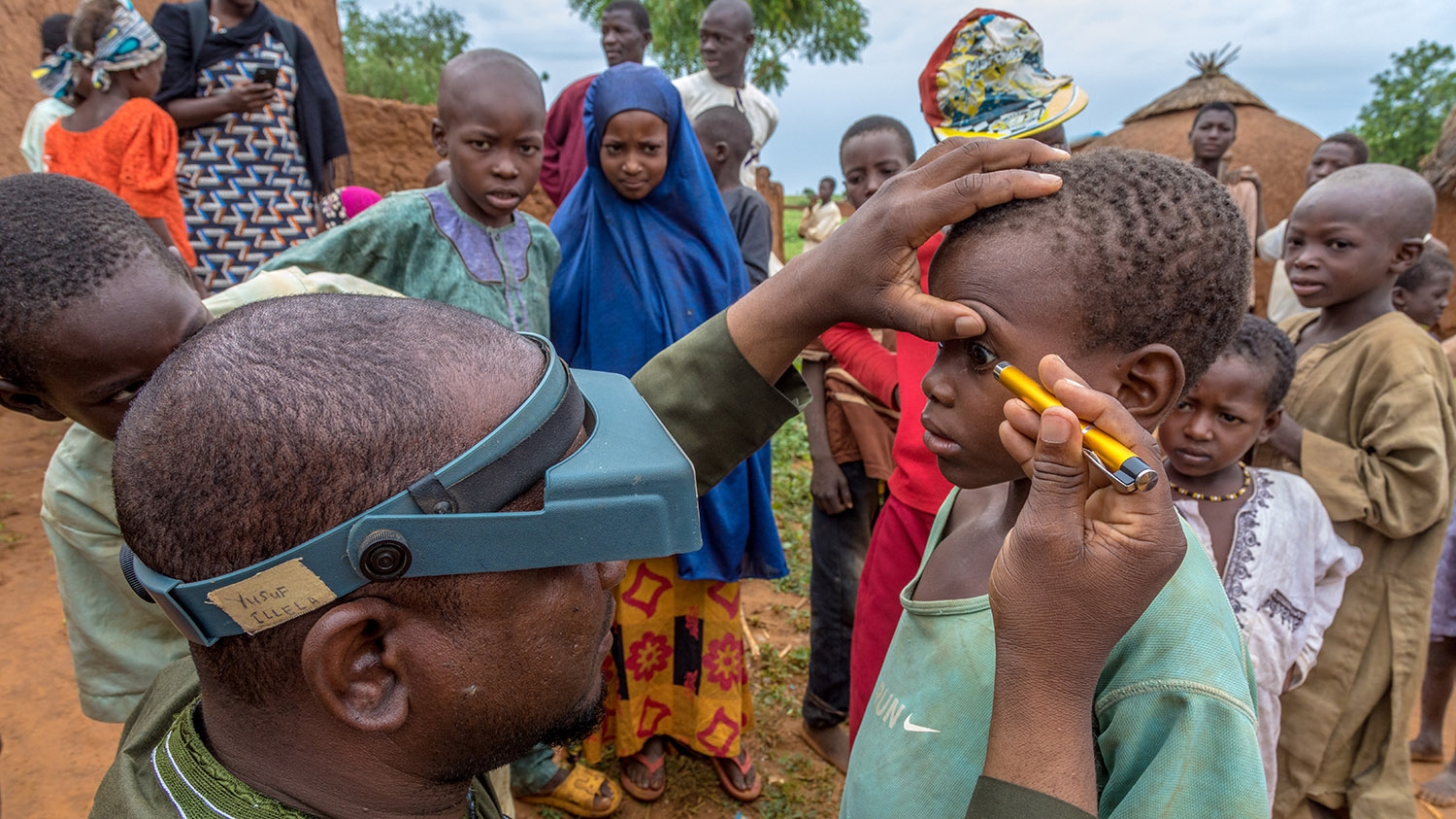 An eye health worker screens a young child for trachoma during a community screening in Sokoto, Nigeria.
