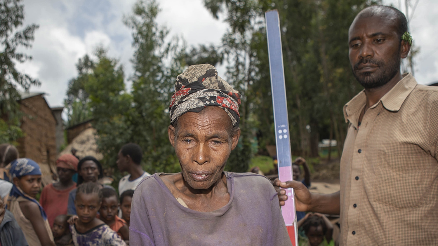 An older woman stands next to a dose pole before receiving medication for trachoma.