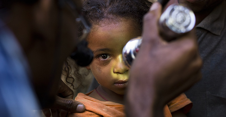 A young child has their eyes examined with a torch.