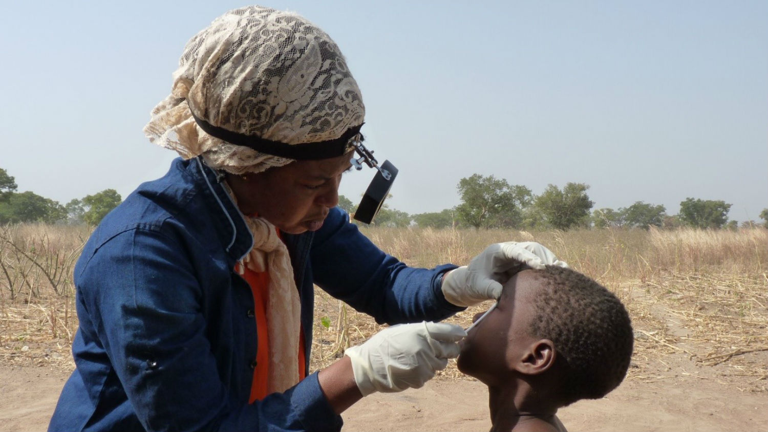 A health worker examines the eyes of a young child outside.