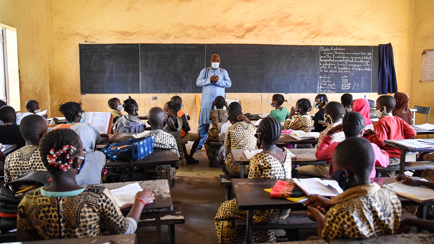 A teacher stands in front of pupils in a classroom.