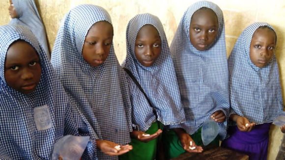 Five girls are holding a hand out showing medication as part of a deworrming project in Nigeria.