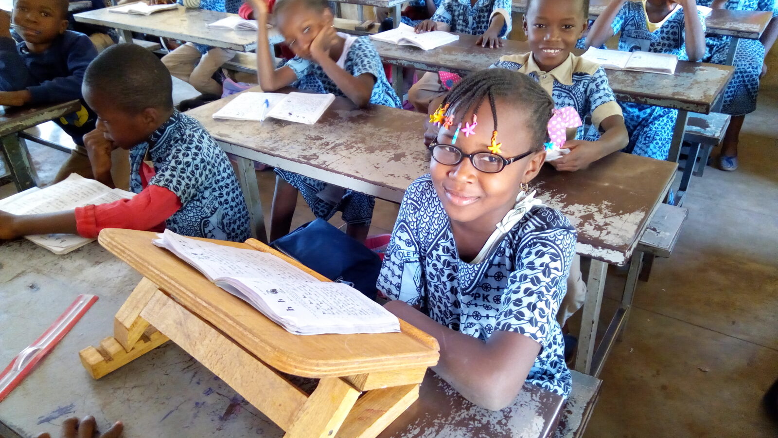 A young girl is sitting at a desk in a classroom with other pupils.