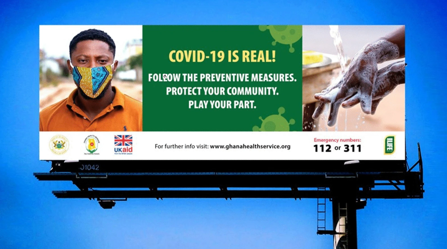 A billboard tells passers-by about how to protect themselves from coronavirus. The billboard includes a picture of a man wearing a mask, and another picture of someone washing their hands.