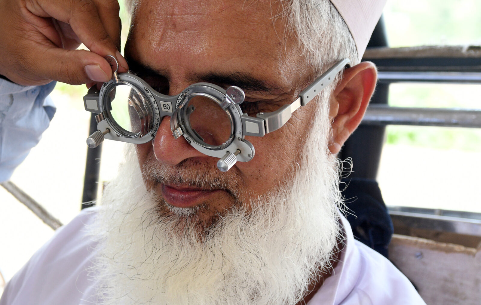An elderly man with a grey beard tries on glasses as part of an eye test.