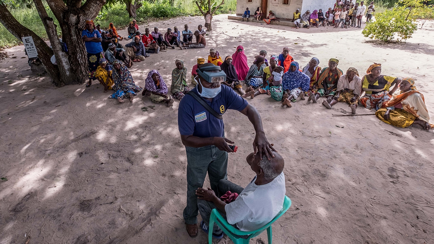 An eye health worker checks a man's eye during an outdoor community screening session in Mozambique.