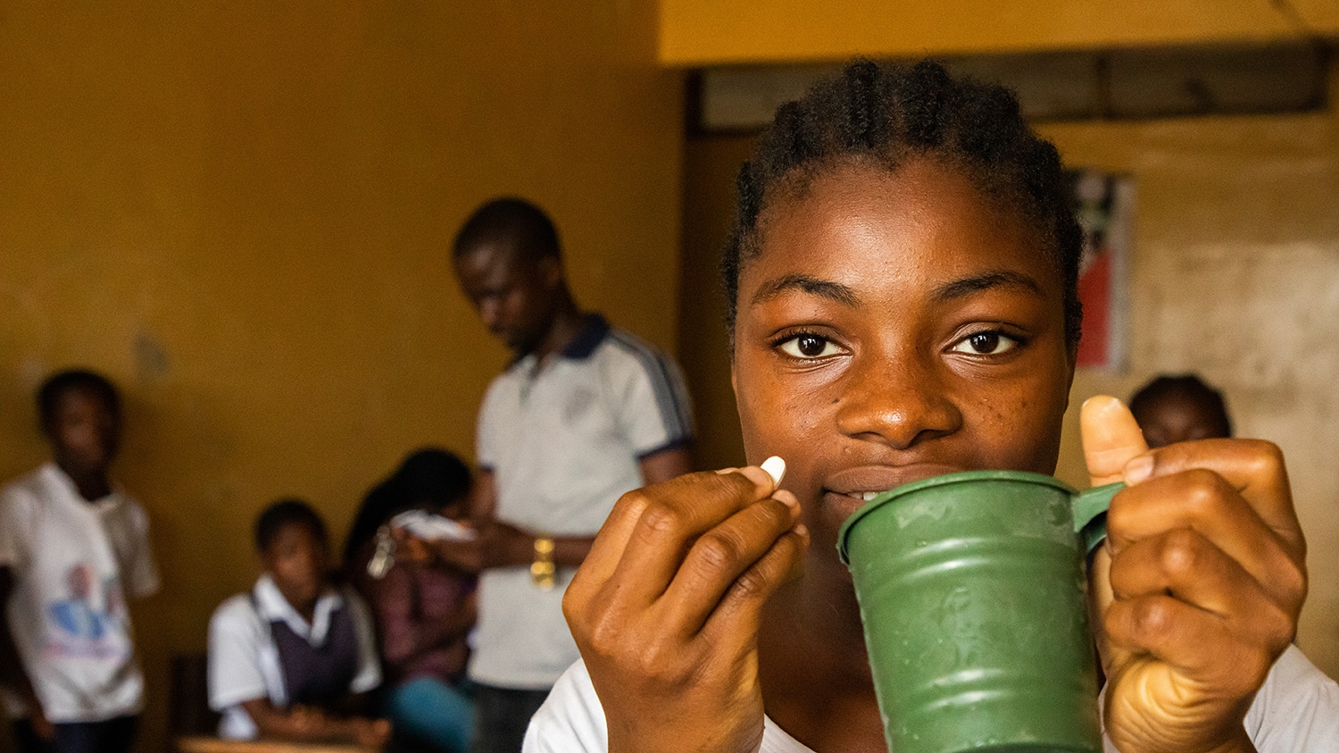 A school girl holds a cup of water in one hand and some medication in the other hand at a mass drug treatment session in Liberia.