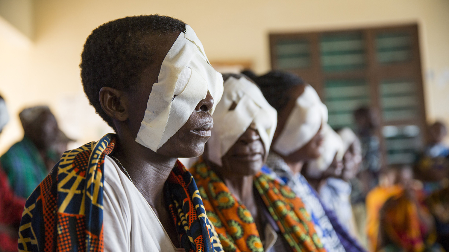 People are sitting in a row with bandages over their eyes after receiving surgery for trachoma.