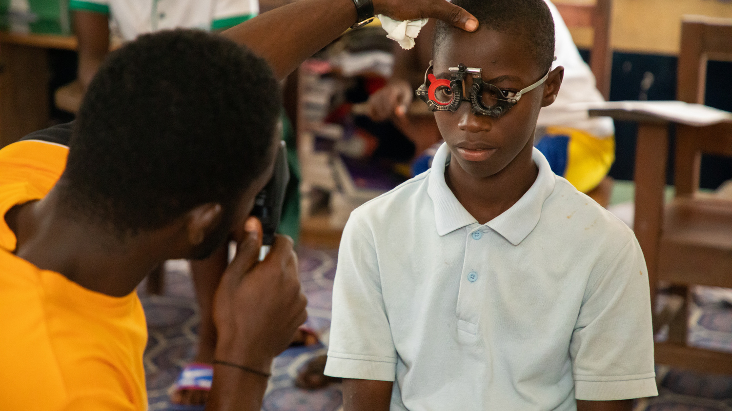 A boy has his eyes screened by a health worker. The boy is wearing a special pair of glasses, and the doctor is examining his eyes.
