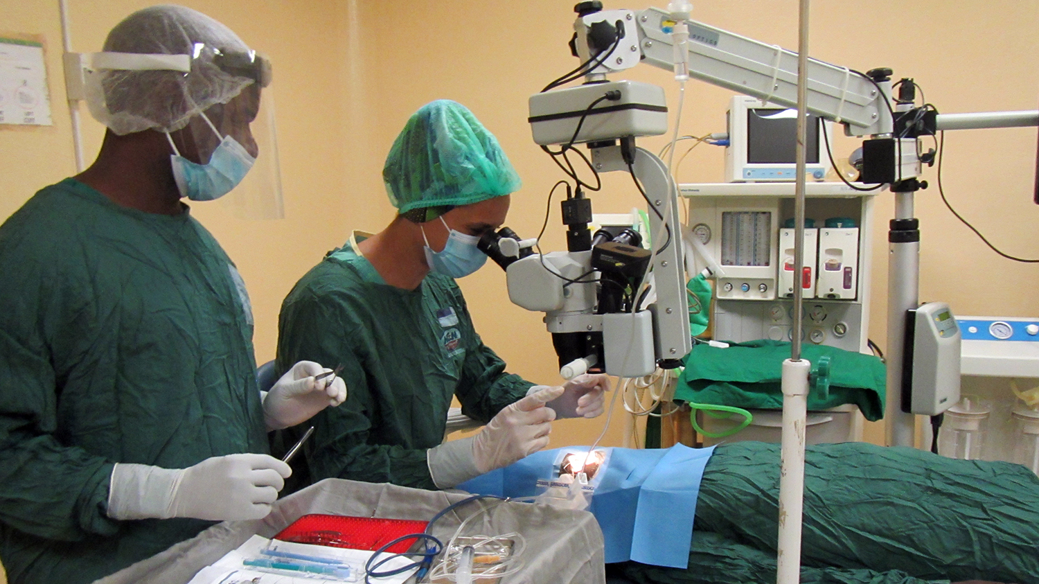 A surgeon, assisted by a nurse, performs cataract surgery on a patient.