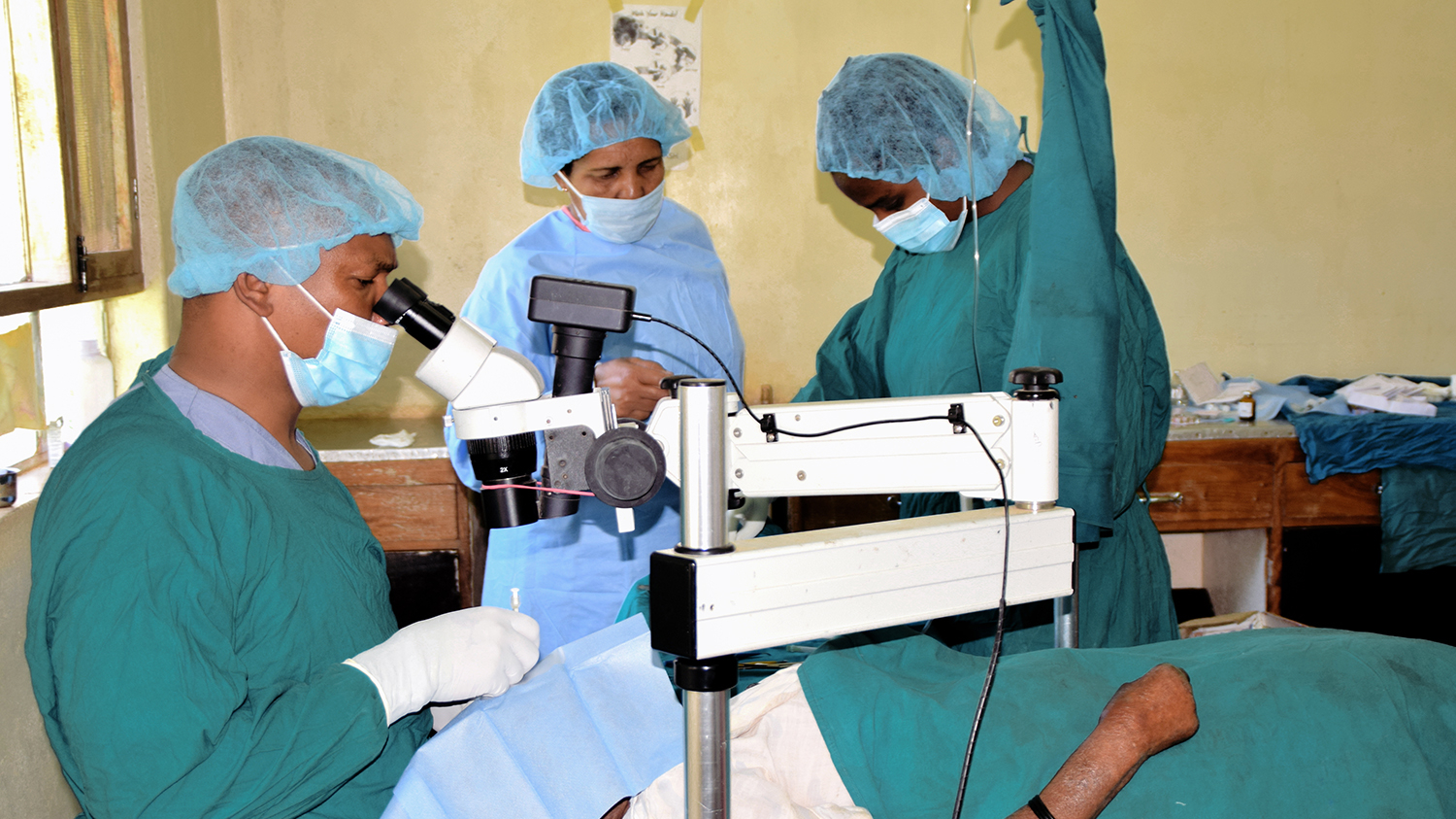 A surgeon performs cataract surgery on a patient, assisted by two eye care workers.