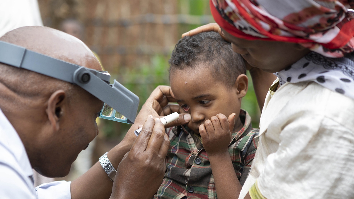 An eye health worker checks a young boy's eyes from signs of trachoma at a community screening session in Ethiopia.