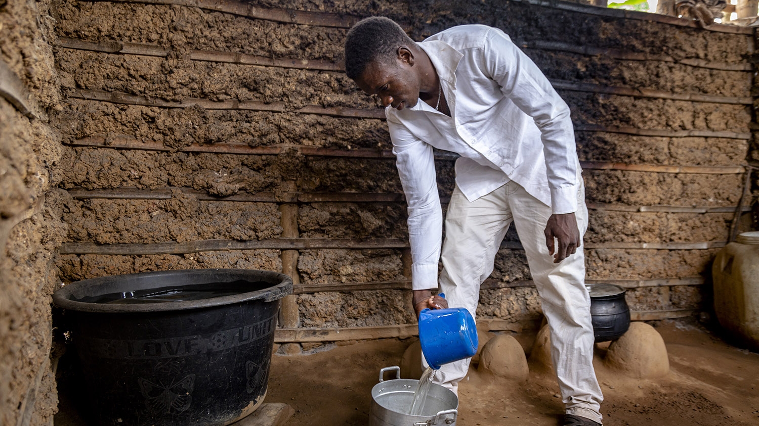 Godfred pours water into a pot at his home.