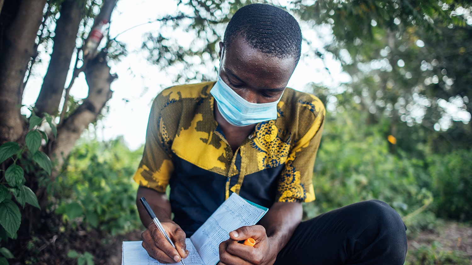 A male researcher wearing a surgical mask writes in a notebook.