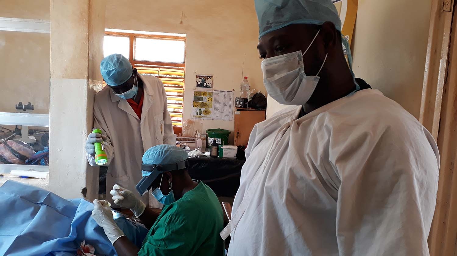 A health worker watches two surgeons perform an operation to treat trachoma.