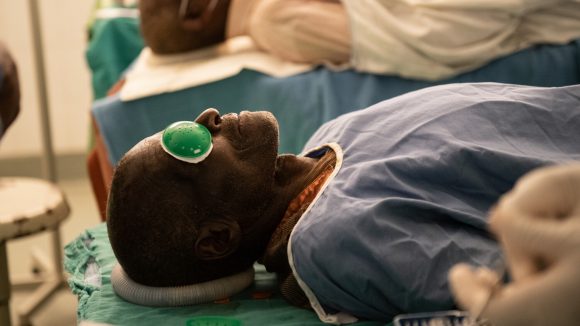 A patient with an eye patch lies on an operating table.